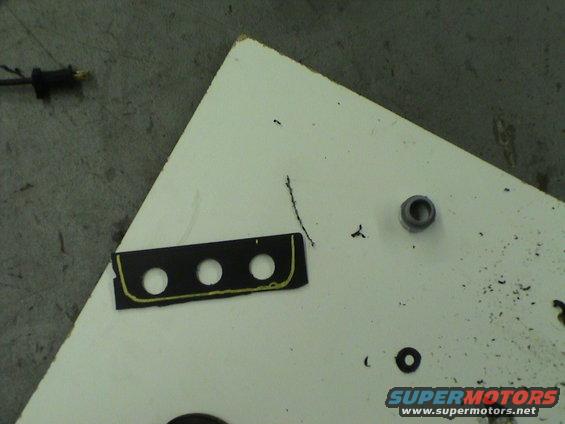 Black plastic trim piece with three circular cutouts and yellow trim, on a white surface