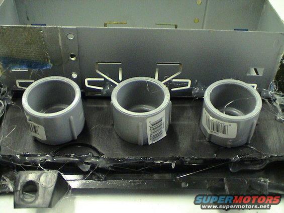 Three PVC pipe fittings attached to a metal bracket, likely for a custom car stereo or gauge setup