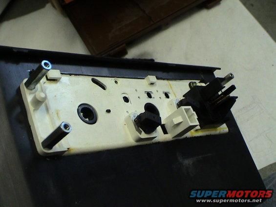 Back of a car's center console assembly with electrical connectors and mounting posts