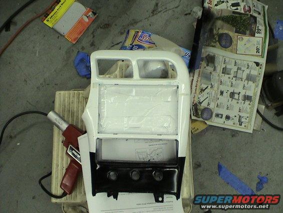 White car interior console with black lower section and three knobs, covered in tape and paper