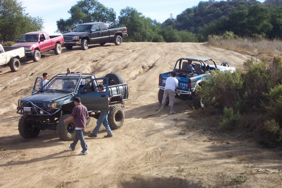 Blue Ford Bronco with a roll cage, being pulled by a rope, on a dirt hill