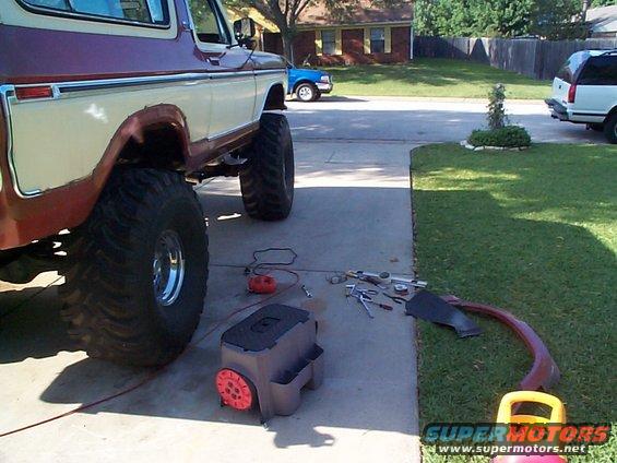 Close-up of a lifted 1978 Ford Bronco's rear fender area with tools and a removed fender trim piece on the ground