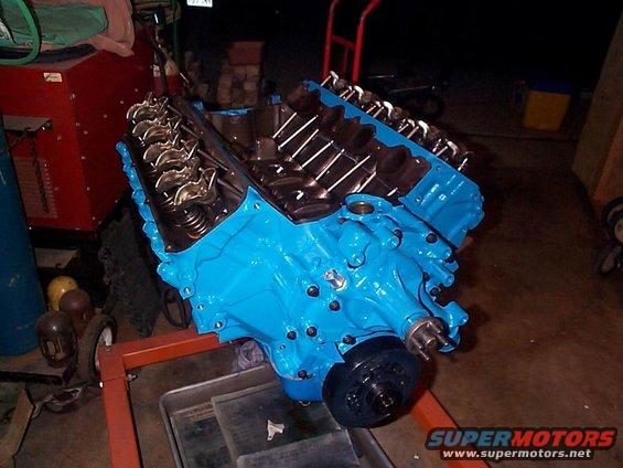 Blue painted V8 engine on an orange stand, showing valve covers and exhaust manifolds
