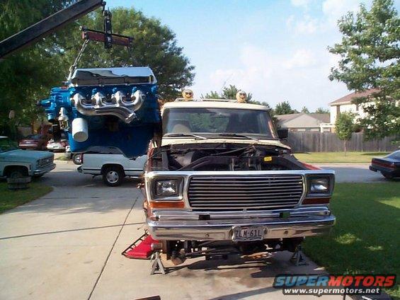 Truck on jack stands with hood up, crane lowering a blue engine into it. License plate ZLM-61L