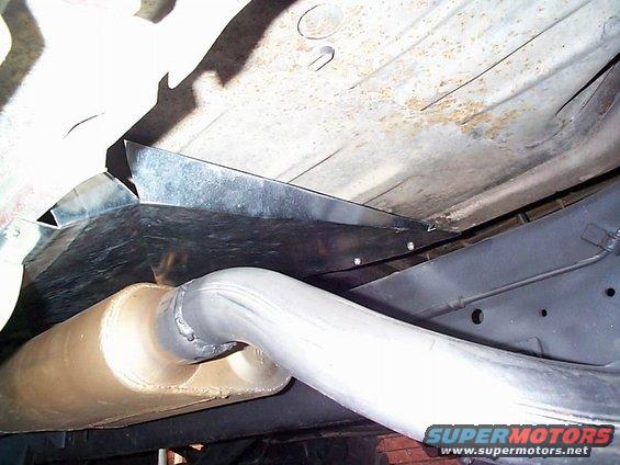 Underside of a vehicle showing the exhaust pipe and muffler, with some metal bracing. Supermotors.net logo visible