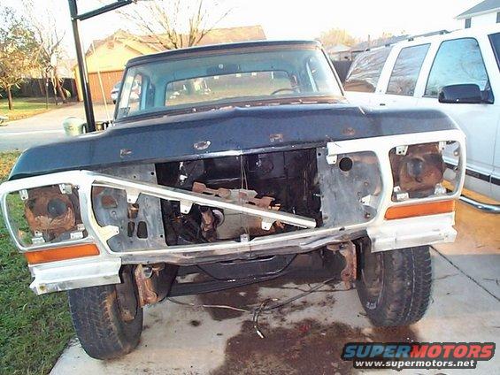 Front end of a 1979 Ford F-Series truck with grille and headlights removed, parked next to a white SUV