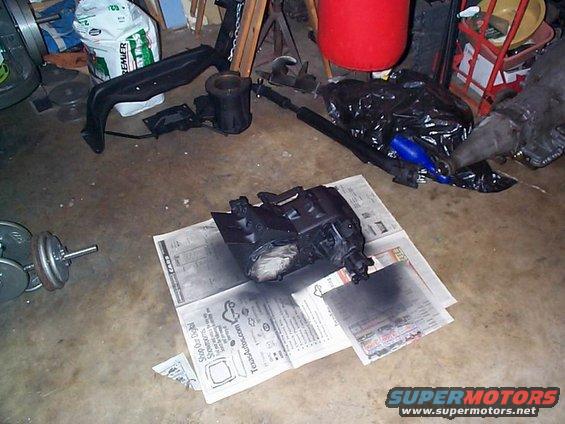 Black automotive part on newspapers, with weights and other car parts in background