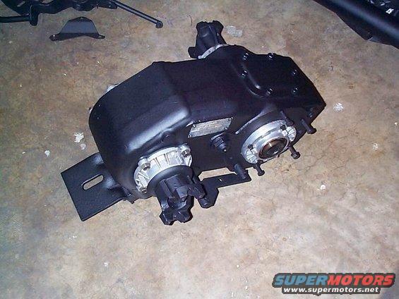 NP205 transfer case with silver output flanges and black housing, sitting on a concrete floor