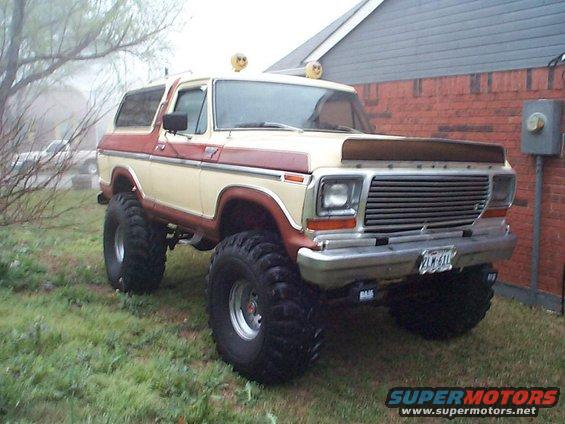 Lifted two-tone beige and red Ford Bronco with large tires parked on grass