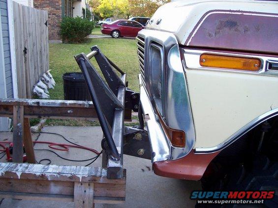 Front of a cream and brown Ford truck with a custom metal bumper attachment. A red car is parked in the background