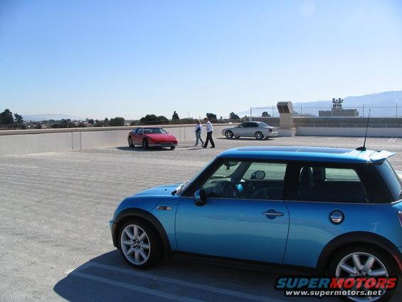 Blue Mini Cooper in foreground, red sports car and silver sedan in background on a sunny day