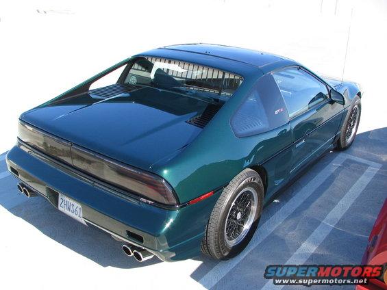 Green 1986 Pontiac Fiero GT with dual exhaust pipes and a GT badge on the rear quarter window