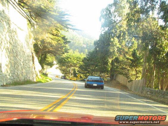 blue sports car driving on a winding road with trees and a stone wall