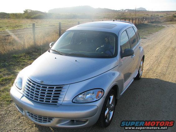 Silver Chrysler PT Cruiser parked on a dirt road with dry grass and a fence in the background