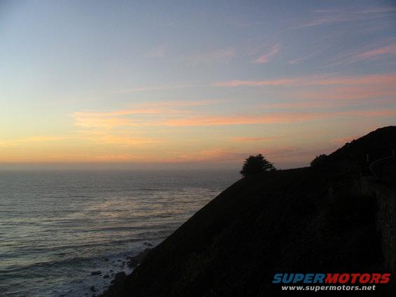 Ocean sunset with pink clouds over a dark cliffside