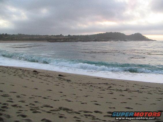 Beach with waves crashing and footprints in the sand under a cloudy sky