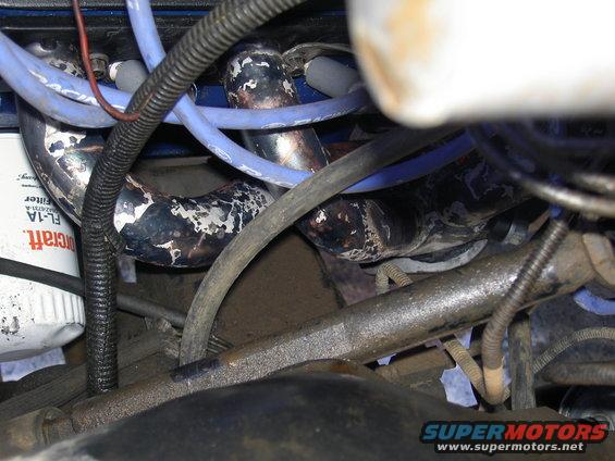 Engine exhaust manifold with peeling paint, blue spark plug wires, and oil filter