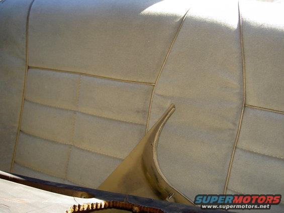 Tan interior rear seat with stitching detail and a curved plastic trim piece