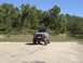 1996 Jeep Cherokee - A tan off-road vehicle with oversized tires sits on a sandy bank next to a body of water.