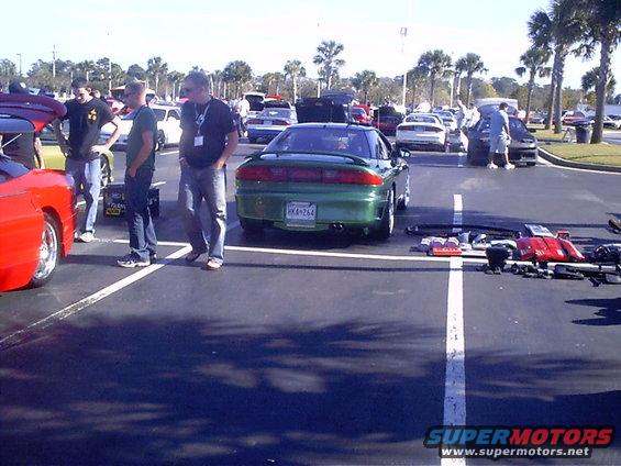 Green coupe parked in lot with people around. Parts laid out on pavement