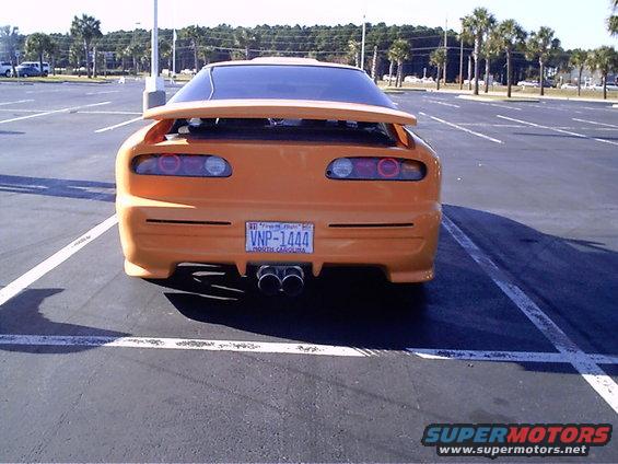 rear view of orange sports car with spoiler and dual exhaust pipes, parked in a lot
