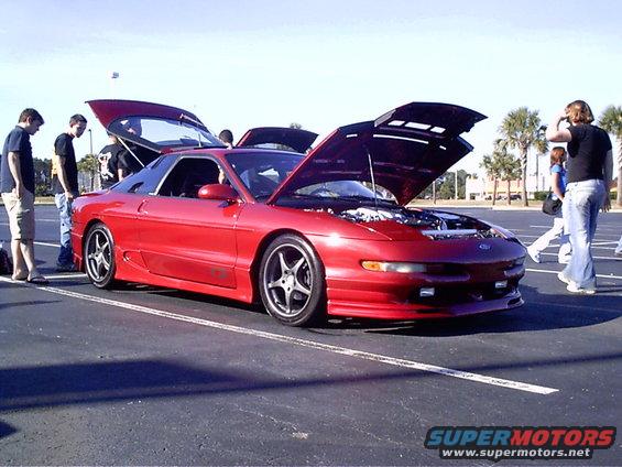 Red 1995 Ford Probe with hoods open, parked in a lot with people around