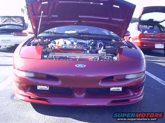 Red Ford Probe with hood open showing engine. Another red car is behind it, and a white car is to the left
