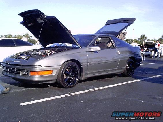 Gray 1995 Ford Probe with hood and trunk open, parked at an outdoor event. Another car is visible to the left