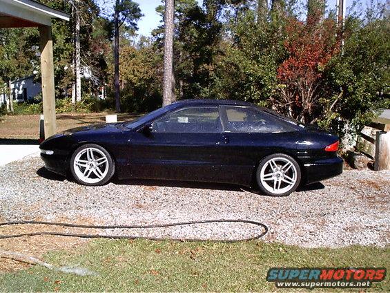 Black 1995 Ford Probe parked on gravel, side view. Has aftermarket wheels