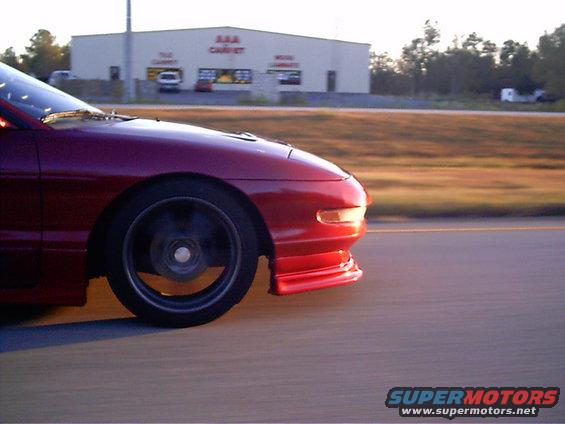 Red 1995 Ford Probe driving on a road, front quarter view. Building in background