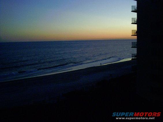 Dark beach scene with ocean waves and a building with balconies at dusk