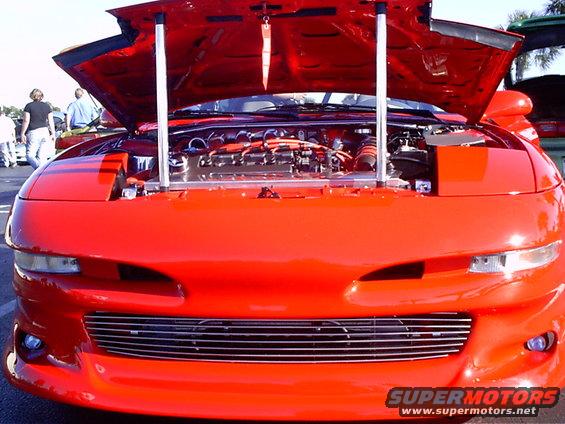 Red 1995 Ford Probe with hood open, showing engine and chrome accents. Front grille is chrome. Headlights are pop-up style