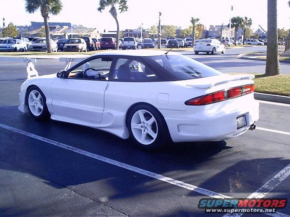 White 1995 Ford Probe with aftermarket body kit and large rear wing, parked in a lot
