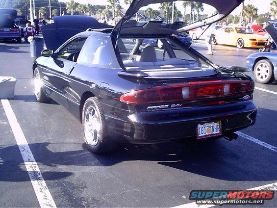 Black 1995 Ford Probe with trunk open, parked at an outdoor event. Other cars visible in background