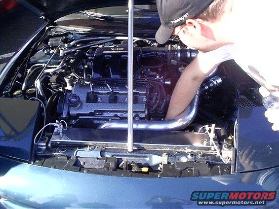 Person working on engine bay, hood open. Aftermarket intake pipe visible