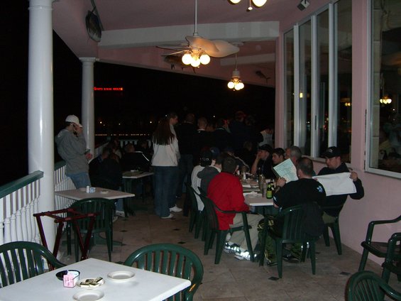 People sit at tables on a covered patio at night, some looking at menus