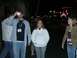 1996 Ford Probe - Group of people gathered outdoors at night with bright lights from buildings in the distance.