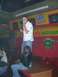 1996 Ford Probe - A man sings into a microphone on a stage, while another person sits nearby. The background features colorful decorations and signs.