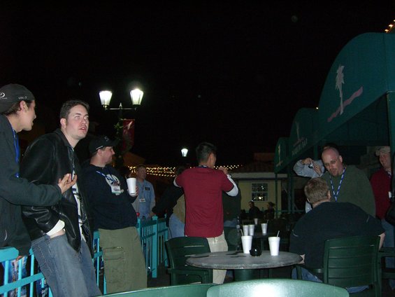 Group of people gathered outdoors at night near a building with a green awning