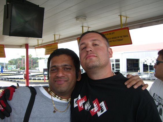 Two guys posing for a photo at a go-kart track. One man has his arm around the other