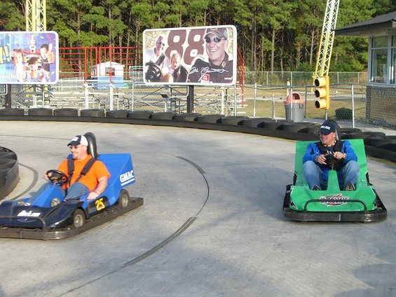 Two go-karts on a track, one blue with number 25, the other green, with a billboard in the background