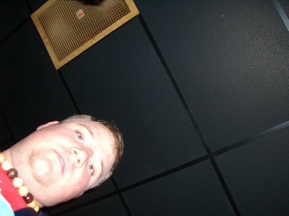 Man wearing a beaded necklace looks up towards a ceiling vent