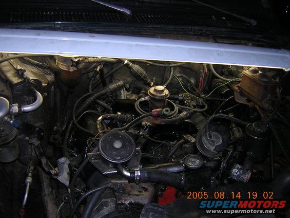 Engine bay with visible hoses, wires, and engine components under bright light