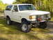 1989 Ford Bronco - A white 1989 Ford Bronco is shown from a 3/4 front view, off-road tires and a custom bumper.