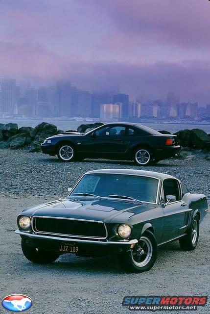 front view of a dark green 1967 Mustang and a black 1999-2004 Mustang behind it, city skyline in background