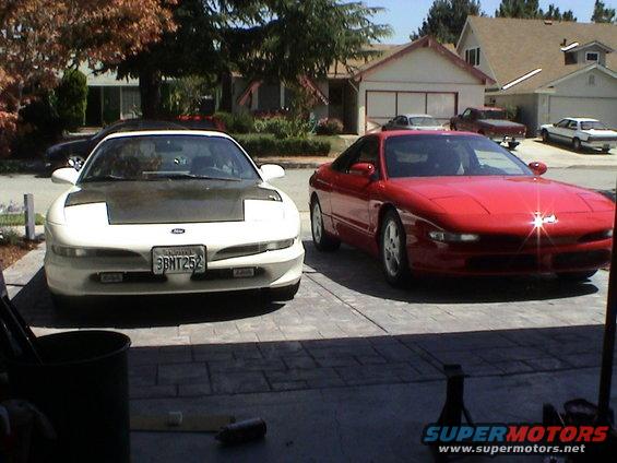Two 1997 Ford Probes, one white with a black hood and one red, parked in a driveway