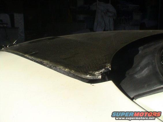 Damaged edge of a carbon fiber car hood, showing frayed material and impact marks