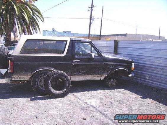 Black Ford Bronco with a white top, missing front passenger wheel, spare tire on rear