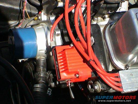 Close-up of an engine's ignition system with red spark plug wires, an orange electronic ignition box, and a blue distributor cap