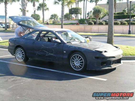 Black 1993 Ford Probe with flame decals and writing on the hood, parked in a lot